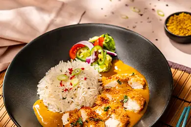 Bowl of rice with Japanese katsu curry, fried chicken, and sliced herb garnish.