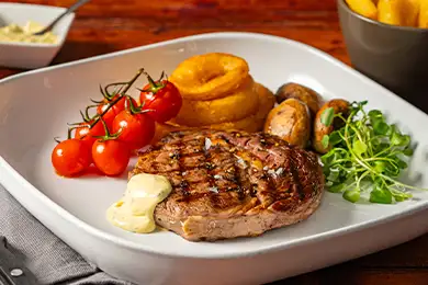 Grilled steak served with onion rings, mushrooms, tomatoes, and chunky chips