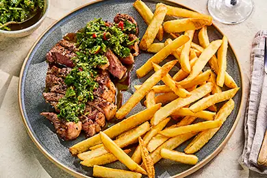 Grilled steak with fries and chimichurri sauce.